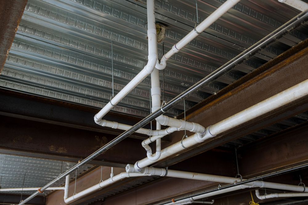White PVC drainage pipes and fittings hung under a steel floor deck